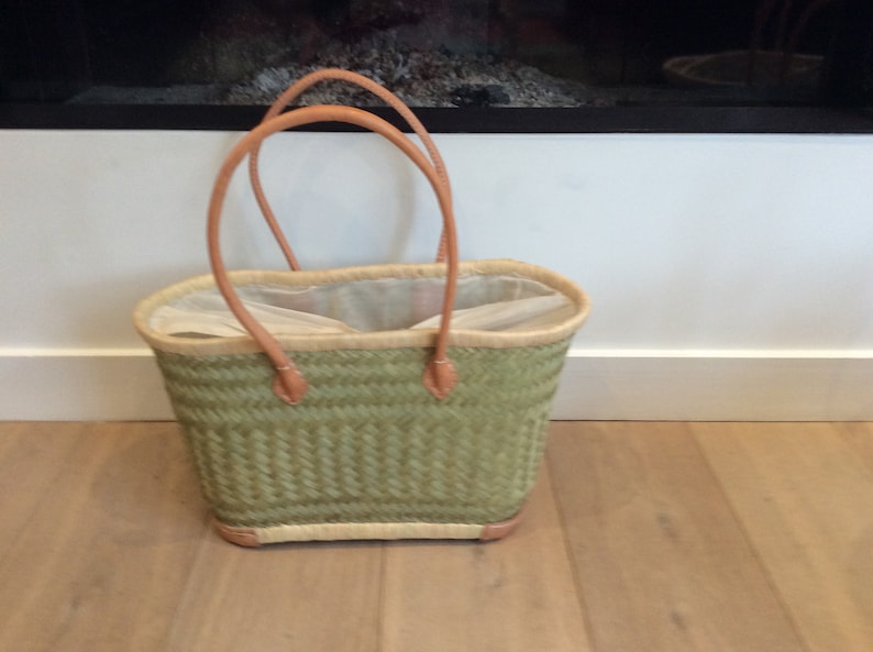 May include: A green woven tote bag with leather handles. The bag is empty and has a white lining.