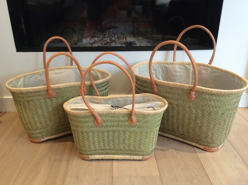 May include: Three green woven baskets with leather handles. The baskets are different sizes and are lined with a white fabric.