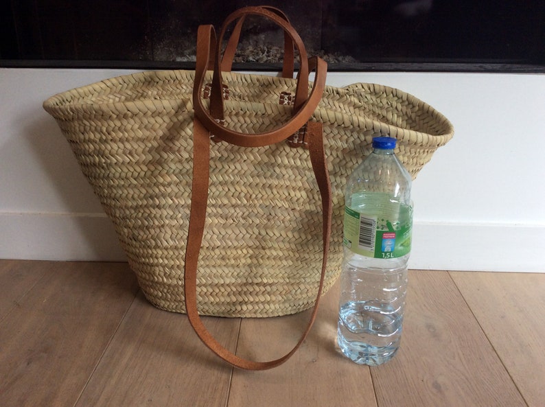 Puede incluir: Un gran bolso de mano de paja trenzada natural con asas de cuero marr&oacute;n. La bolsa est&aacute; al lado de una botella de agua de pl&aacute;stico transparente con una tapa azul. La botella est&aacute; etiquetada con "1,5L".