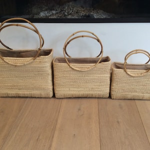 Peut inclure: Trois paniers rectangulaires tressés de différentes tailles. Chaque panier a un corps tissé brun clair, une doublure beige et des anses en bambou. Les paniers sont disposés du plus grand au plus petit, le plus grand étant à gauche.