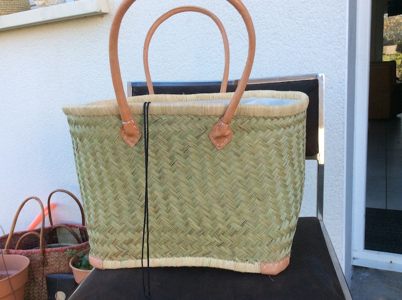 May include: A woven green basket with leather handles. The basket has a light brown trim and a black drawstring.