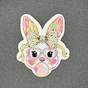May include: A white bunny with pink ears and a black and white polka dot bow. The bunny is wearing heart-shaped glasses and blowing a pink bubble.