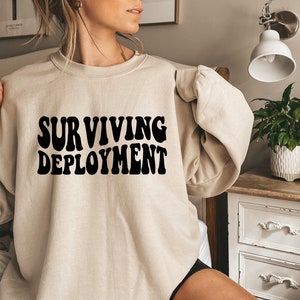 May include: A beige sweatshirt with the text "SURVIVING DEPLOYMENT" printed in black.