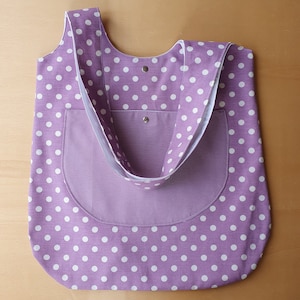 May include: A purple tote bag with white polka dots. The bag has a large pocket on the front and a single strap.