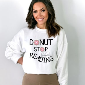 May include: White sweatshirt with a black graphic that says "Donut Stop Reading" with a pink donut and a book illustration.