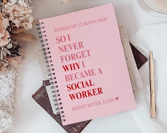 May include: A pink spiral-bound notebook with the text "THINGS MY CLIENTS SAID" and "SO I NEVER FORGET WHY I BECAME A SOCIAL WORKER." A gold pen and a glass of liquid are also visible.