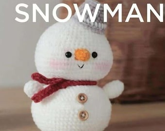 Peut inclure: Un bonhomme de neige en crochet blanc avec une écharpe rouge, un chapeau gris et deux boutons marrons. Le bonhomme de neige a un petit nez orange et des yeux noirs.