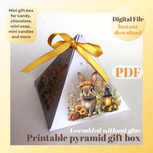 May include: Printable PDF template for a pyramid-shaped gift box. The box features a cute bunny illustration with a floral design and a yellow ribbon. The text "Assembled without glue" and "Printable pyramid gift box" is included on the image.