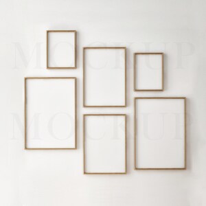 May include: Five gold picture frames of different sizes are arranged on a white wall. The frames are empty and ready for photos or artwork.