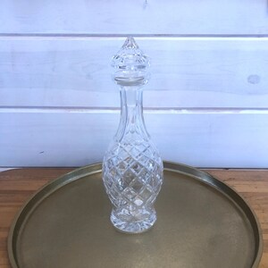 May include: A clear glass decanter with a diamond pattern and a stopper on a gold tray.