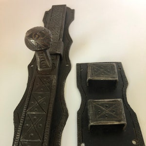 May include: A pair of antique iron door latches with intricate designs. The latch on the left has a round knob and a decorative pattern. The latch on the right has two rectangular plates with a similar pattern.