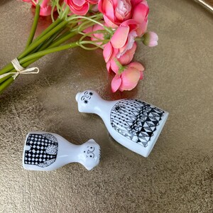 May include: A pair of white ceramic salt and pepper shakers with black and white geometric designs. The shakers are shaped like people and have faces.