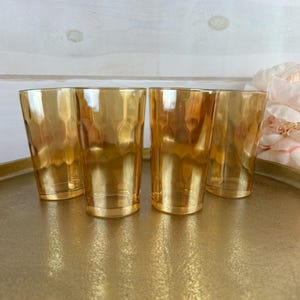 Puede incluir: Cuatro vasos de color ámbar con una superficie texturizada están colocados sobre una bandeja dorada. Una flor rosa claro está en el fondo. Los vasos tienen un patrón de panal.