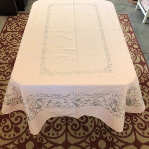 May include: White tablecloth with a gray floral pattern border. The tablecloth has a scalloped edge.