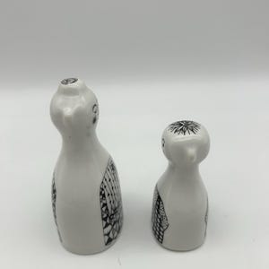 May include: A set of two white ceramic salt and pepper shakers with black and white patterned designs. The shakers are shaped like birds.