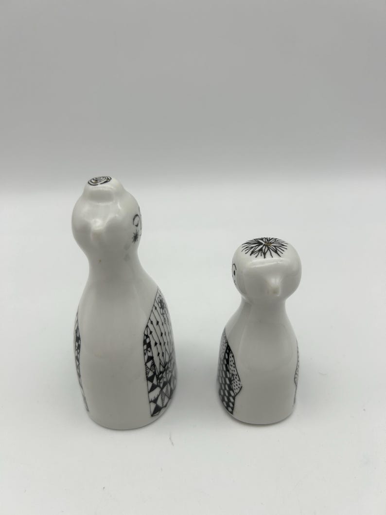 May include: A set of two white ceramic salt and pepper shakers with black and white patterned designs. The shakers are shaped like birds.