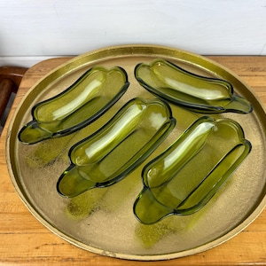 May include: Four green glass dishes shaped like hot dog buns on a gold tray.