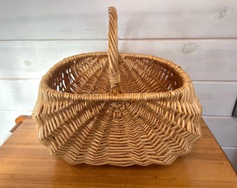 May include: A woven wicker basket with a sturdy handle. The basket has a square shape with rounded edges and a textured pattern. The natural tan color of the wicker gives it a rustic, farmhouse aesthetic. The handle is firmly attached.