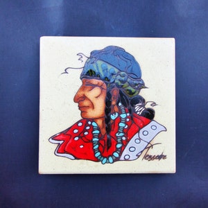 May include: A ceramic tile with a painted image of a Native American man wearing a blue and green headdress and a red shirt with turquoise beads. The tile is signed "Tessare" in the bottom right corner.