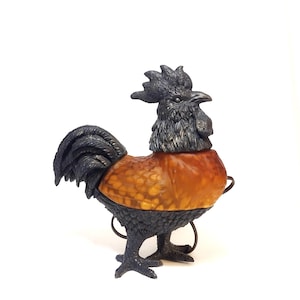 May include: A decorative rooster figurine with a black head, tail, and legs, and a brown and orange body. The rooster has a detailed, textured appearance and is set against a white background.
