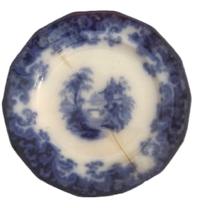 May include: Antique blue and white porcelain plate with a landscape scene in the center. The plate has a scalloped edge and a decorative border. The plate is likely vintage and shows signs of wear.