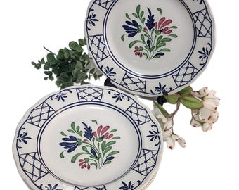 May include: White ceramic plates with a blue and white geometric border and floral center design. The floral design features blue, green, and pink flowers. The plates have a scalloped edge.