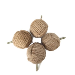 Könnte beinhalten: Vier braune Seil-Schrankknöpfe mit Metallschrauben. Die Knöpfe sind aus natürlichem Juteseil gefertigt und haben einen rustikalen, ländlichen Stil.
