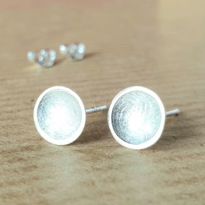 May include: A pair of silver stud earrings with a textured, circular design. The earrings are small and delicate.