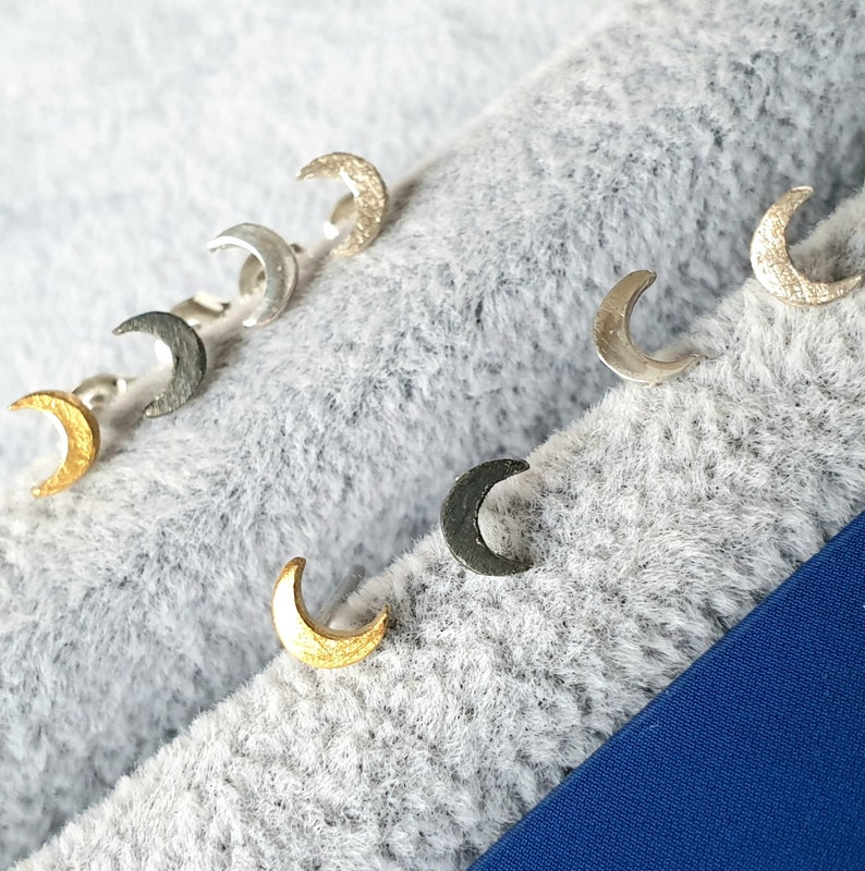 May include: A set of six crescent moon earrings in various finishes, including gold, silver, and black. The earrings are displayed on a gray fuzzy surface.