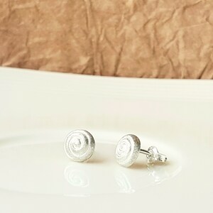 May include: A pair of silver stud earrings with a spiral design. The earrings are small and delicate, and they would make a great gift for a friend or loved one.