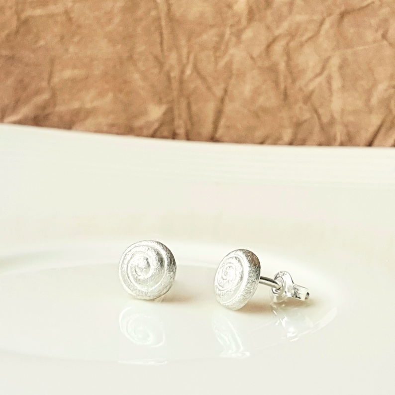 May include: A pair of silver stud earrings with a spiral design. The earrings are small and delicate, and they would make a great gift for a friend or loved one.