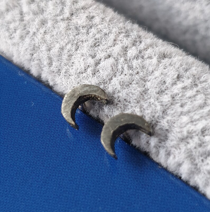 May include: A pair of silver crescent moon earrings. The earrings are small and delicate, and they have a slightly textured surface.