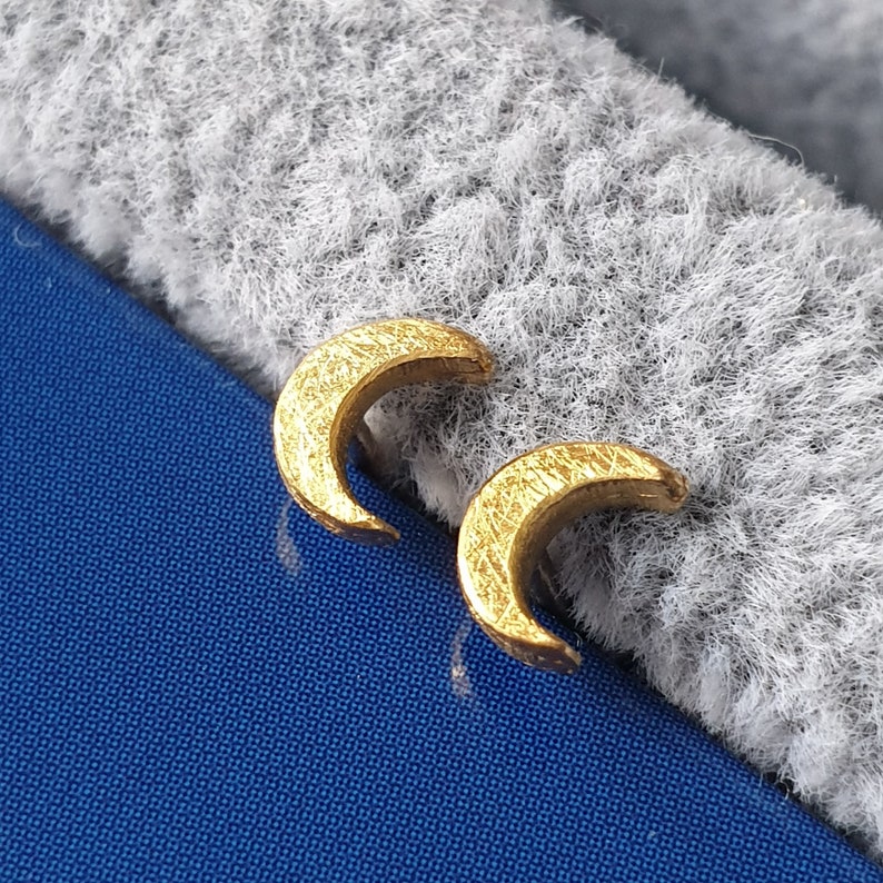 May include: A pair of gold crescent moon earrings. The earrings are small and delicate, with a textured surface.