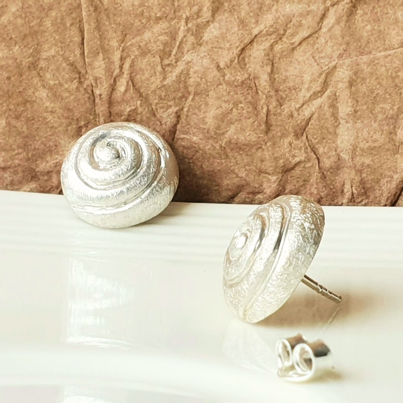 May include: A pair of silver earrings with a textured, spiral design. The earrings are in the shape of a shell.