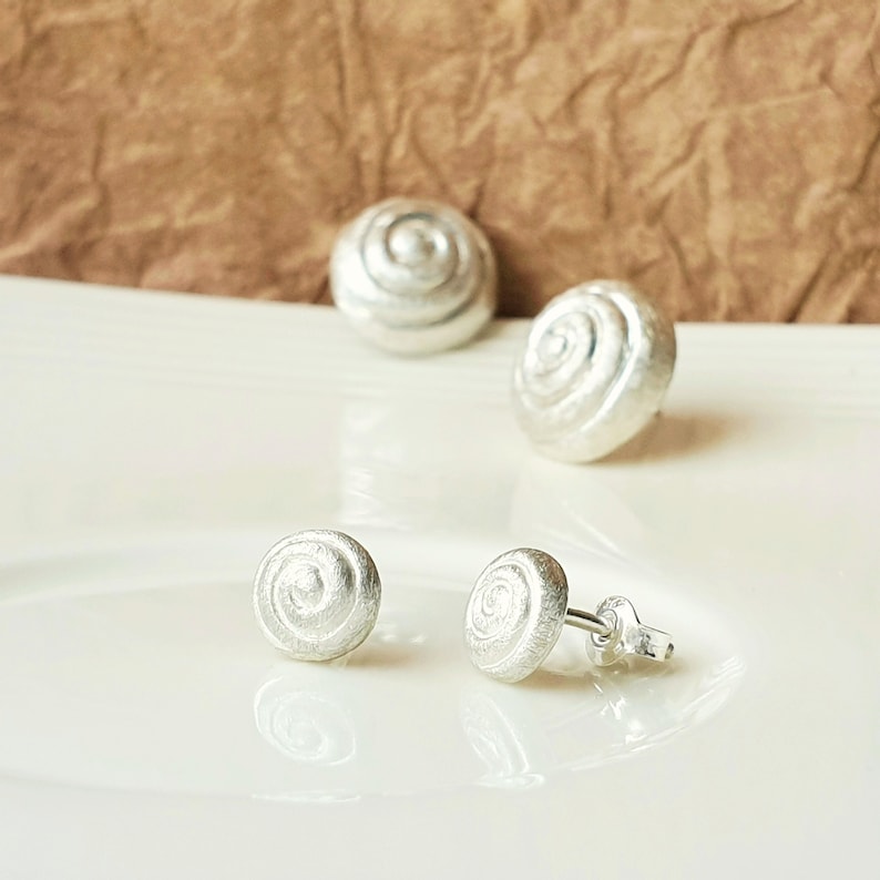 May include: A set of four silver earrings with a spiral design. The earrings are small and delicate, and they would make a great gift for a friend or loved one.