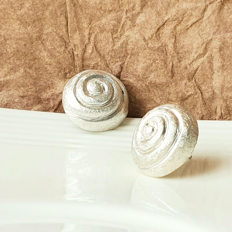 May include: A pair of silver earrings with a spiral design. The earrings are round and have a textured surface.