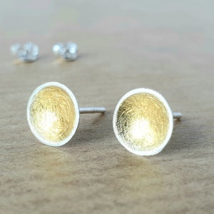 May include: A pair of silver stud earrings with a gold-toned, textured, circular design.