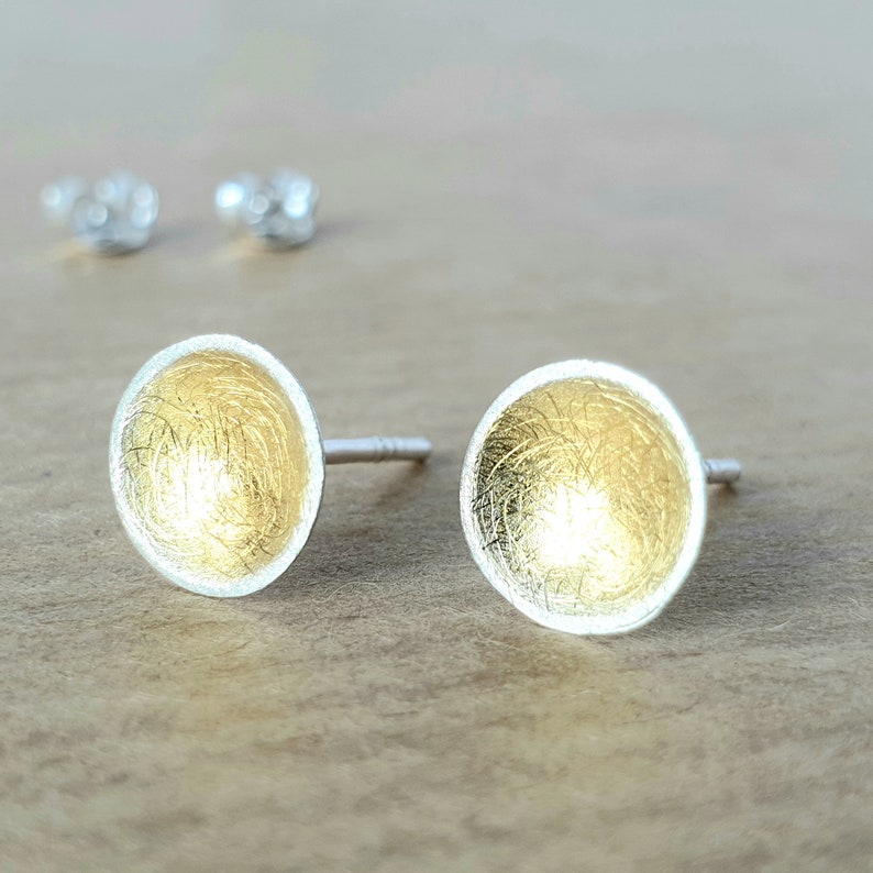 May include: A pair of silver stud earrings with a gold-toned, textured, circular design.