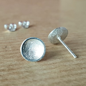 May include: Two silver earring studs, one with a round, flat, textured surface and the other with a post and a backing.