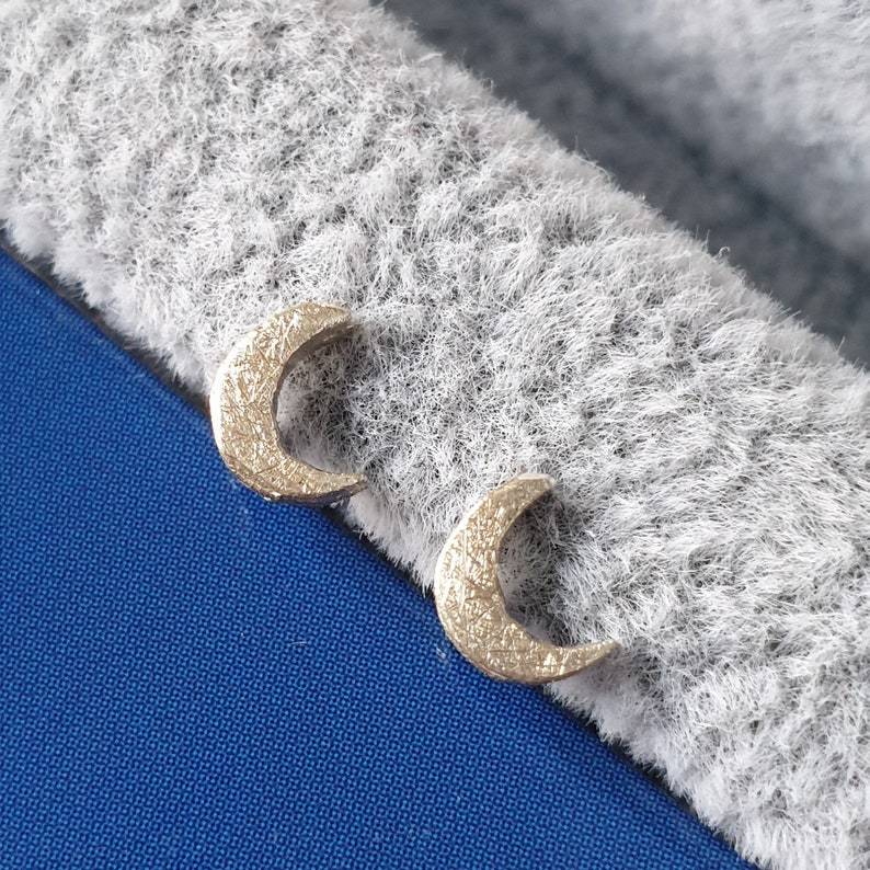 May include: A pair of gold crescent moon earrings. The earrings are small and delicate, and they have a textured surface.