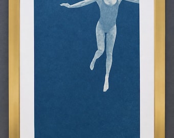May include: A cyanotype print in a gold-colored frame featuring a white silhouette of a figure in a one-piece swimsuit floating against a deep blue background. The artwork is signed and dated 2016 in the bottom right corner of the print.