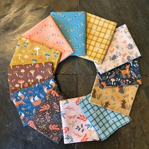 May include: A collection of folded fabric squares arranged in a circular pattern. The fabrics feature various nature-themed patterns, including mushrooms, foxes, floral designs, and plaid. Colors include pink, blue, yellow, brown, and teal, creating a vibrant and whimsical aesthetic.