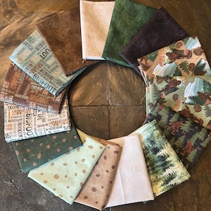 May include: A collection of fabric squares in various colors and patterns. Some fabrics feature text with words like "Bigfoot" and "Sasquatch." Other fabrics have forest and mountain scenes, and some have a speckled design.
