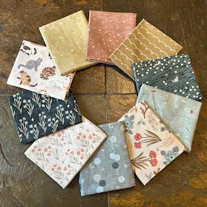 May include: A collection of folded fabric squares with various patterns, including cats, floral designs, and abstract shapes. The color palette includes shades of green, pink, yellow, and gray. The fabrics are arranged in a circular pattern.