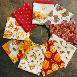 May include: A collection of eight fabric squares featuring autumnal themes. The squares feature various designs including pumpkins, acorns, leaves, turkeys, and a birdhouse. The fabrics are in shades of red, orange, yellow, brown, and white.