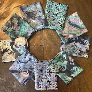 May include: A collection of ten folded fabric squares arranged in a circular pattern. The fabrics feature various fantasy-themed designs, including dragons, Celtic knots, and swirling patterns in shades of blue, green, and purple.