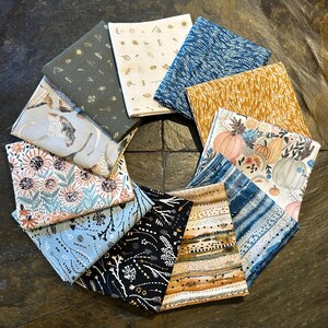 May include: A circular arrangement of folded fabric squares with various patterns. The fabrics feature floral, botanical, and abstract designs in colors like blue, gold, gray, and cream. Some fabrics have pumpkin and sunflower motifs.