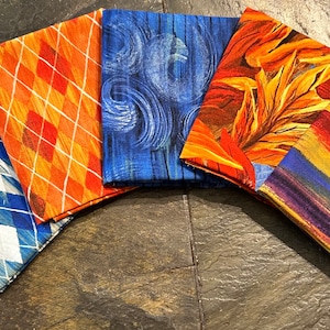 May include: Five fabric squares with different patterns. The squares are in shades of blue, orange, and yellow. The patterns include a diamond pattern, a swirling pattern, a leaf pattern, a striped pattern, and a brushstroke pattern.