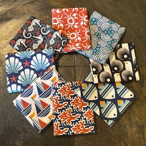 May include: Eight different fabric squares with nautical themed patterns. The patterns include seahorses, seashells, coral, fish, boats, and waves. The fabrics are in shades of blue, red, white, and black.
