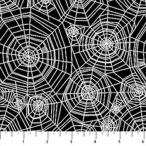 May include: A black and white fabric featuring a repeating pattern of spiderwebs. The webs are white and intricately designed, contrasting sharply against the black background. The image includes a ruler along the bottom, showing measurements in inches.